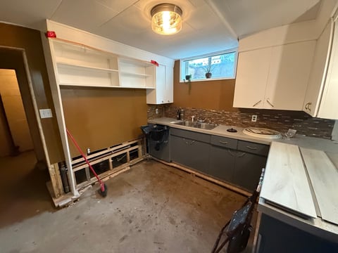 Kitchen under renovation with exposed walls, concrete floor, stove, counter, and partial cabinetry installation