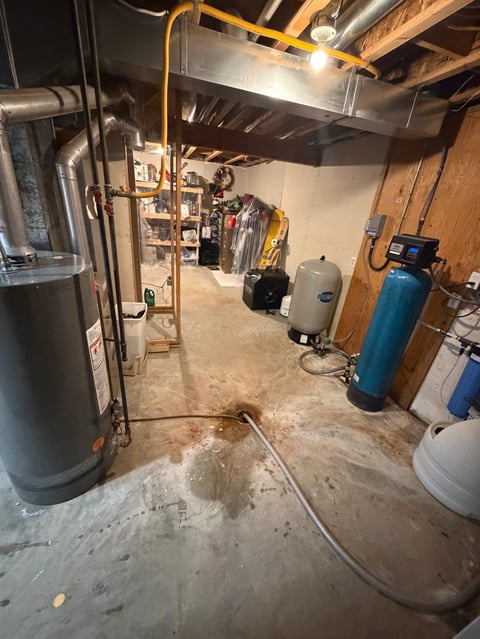 Basement utility room with water heater, yellow pipes, storage shelves, blue water filtration tanks, and concrete floor