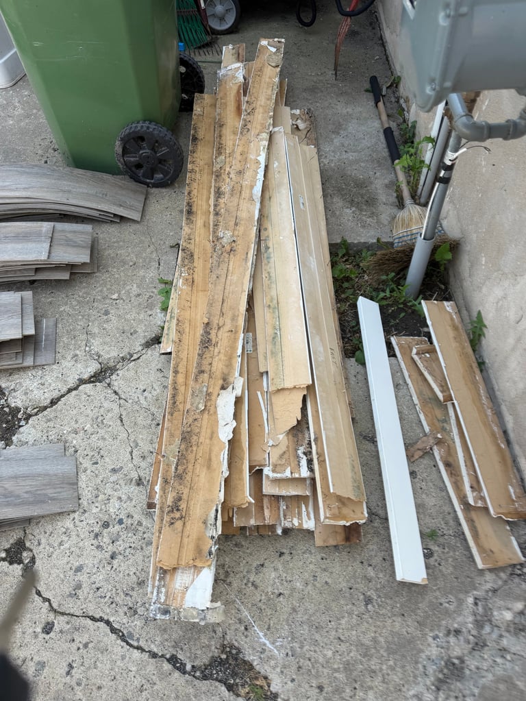Overhead view of stacked wooden planks and lumber pieces on concrete ground in storage area with green bins and tools nearby
