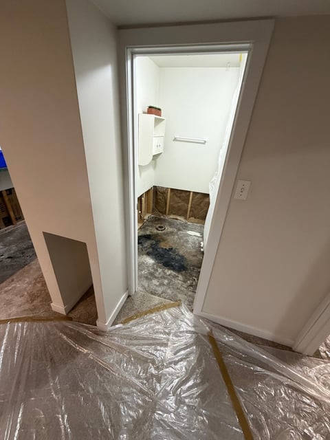 Doorway to a bathroom under renovation with plastic floor protection and exposed flooring visible inside