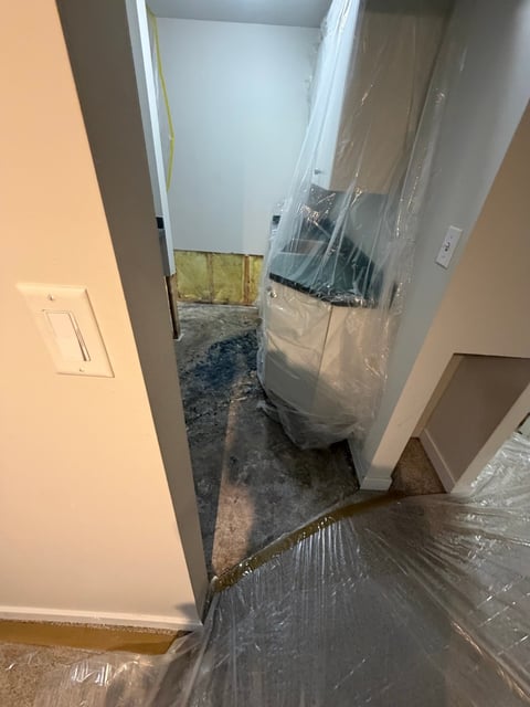 Interior hallway under renovation with plastic sheeting protecting doorway and debris on floor.