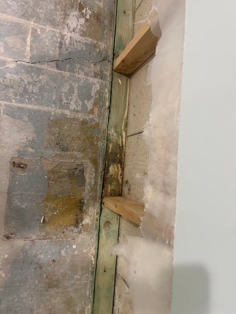 Deteriorated brick wall with green metal frame and wooden shims showing water damage and decay
