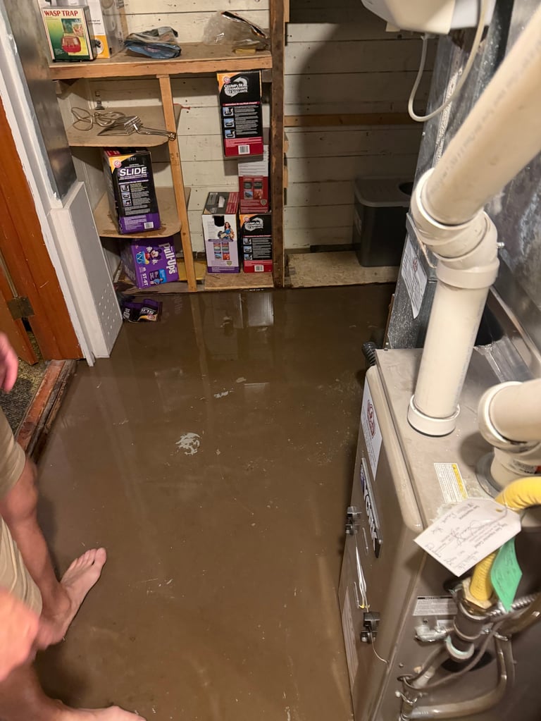 Flooded basement with murky brown backup water covering the floor, shelving with stored items, HVAC equipment, and PVC pipes visible